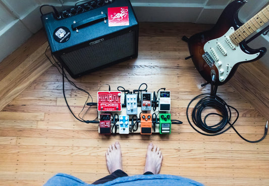 Guitar pedalboard with assorted analog effects pedals alongside an electric guitar and amplifier