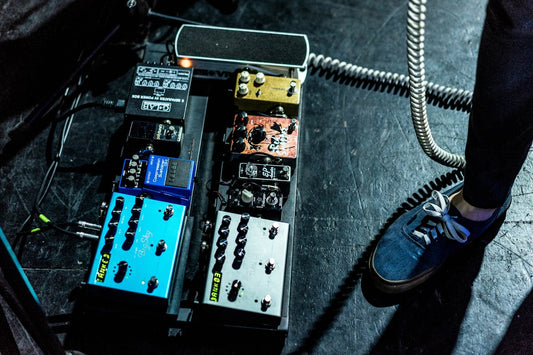 Guitar pedalboard setup with colorful effects pedals on stage, shot from above