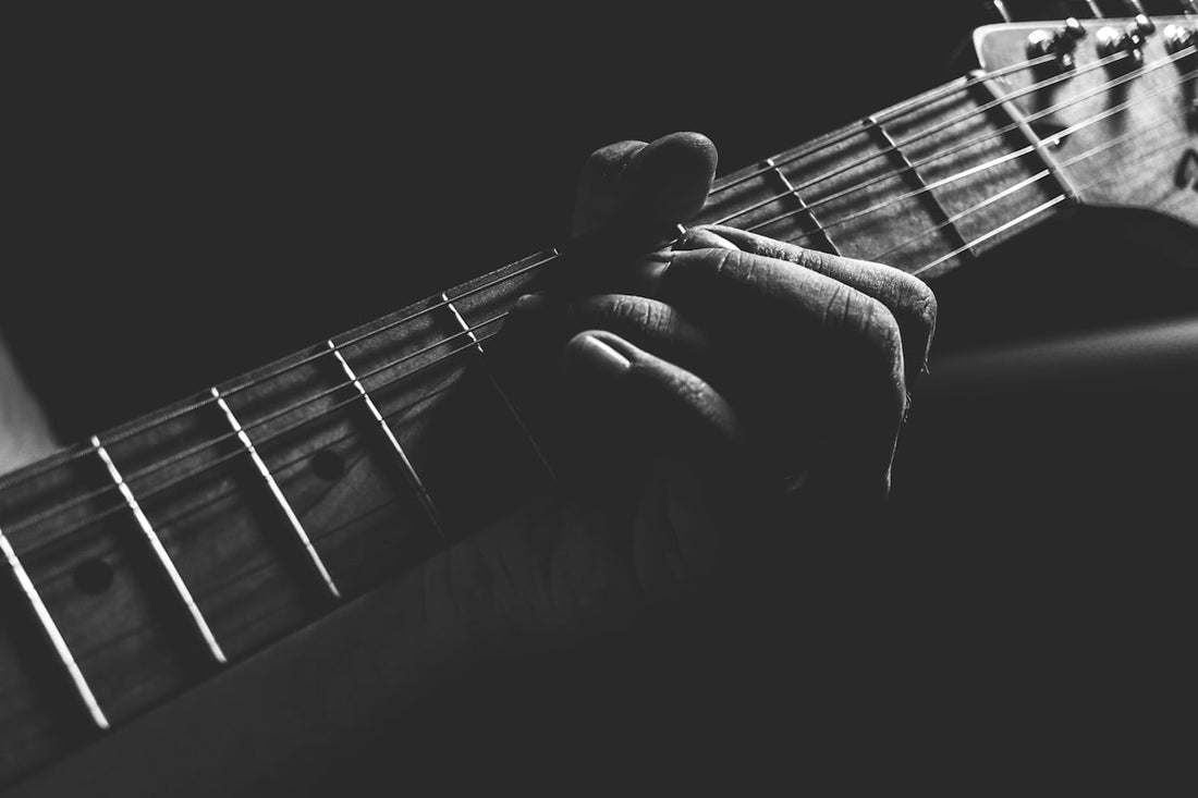 Close-up of a guitarist's hand fretting an electric guitar in moody black and white lighting
