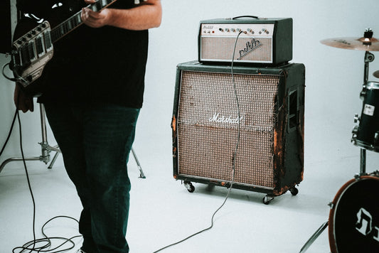 Guitarist standing next to a vintage Marshall tube amp half-stack in a studio setting