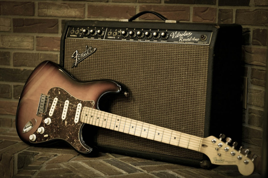 Fender Stratocaster electric guitar leaning against a vintage Fender tube amplifier in a studio setting