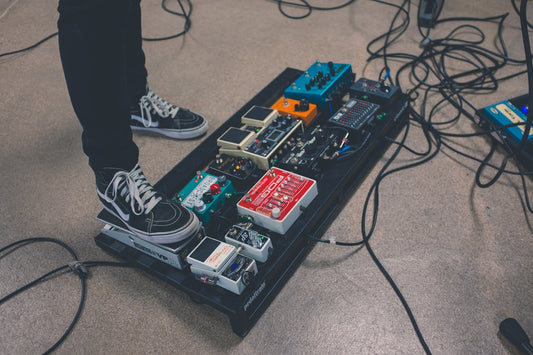 Guitar pedalboard on stage with multiple effects pedals and cables during a live performance